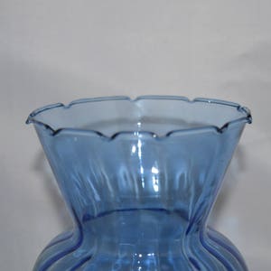 May include: A light blue glass vase with a scalloped rim and vertical ridges. The vase is empty.