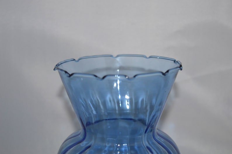 May include: A light blue glass vase with a scalloped rim and vertical ridges. The vase is empty.
