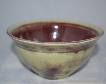 May include: A large, ceramic bowl with a light green glaze and a dark red glaze. The bowl has a wide rim and a rounded bottom.