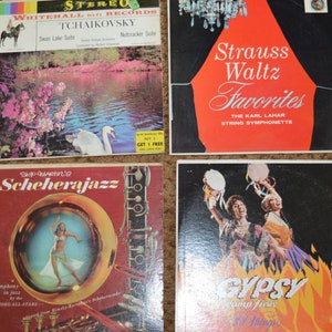 Pode incluir: Quatro álbuns de discos de vinil vintage. Os títulos incluem "Swan Lake Suite", "Strauss Waltz Favorites", "Scheherajazz" e "Gypsy Camp Fires". As capas dos álbuns apresentam ilustrações e texto em várias cores, incluindo vermelho, branco e preto.