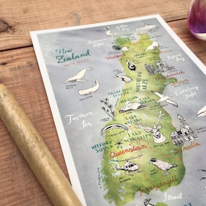 May include: A hand-drawn map of New Zealand with watercolor details. The map features the South Island with the Southern Alps, Franz Josef Glacier, Milford Sound, Queenstown, and Invercargill. The North Island is not shown. The map is on a white background with a light blue watercolor wash.
