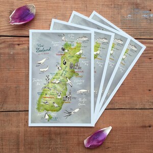 May include: A set of five illustrated postcards featuring a map of New Zealand with various animals and landmarks. The postcards are printed on a light blue background with a watercolor effect.