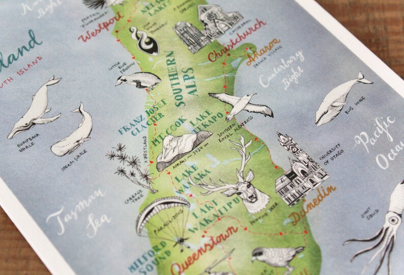 May include: A watercolor illustration of the South Island of New Zealand, featuring landmarks like Franz Josef Glacier, Mount Cook, Lake Wanaka, and Queenstown. The illustration includes a variety of animals, including whales, a deer, and a bird. The text "South Island" is written in the top left corner of the illustration.