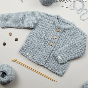 May include: A knitting pattern for a baby cardigan, featuring a light blue knitted cardigan with wooden buttons, a ball of light blue yarn, and knitting needles. The pattern is titled "Lilly Baby Cardigan Knitting Pattern".
