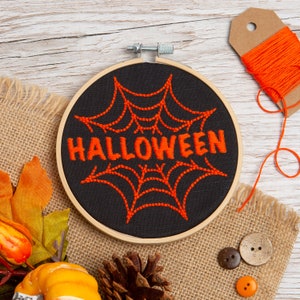 May include: A black embroidery hoop with an orange spiderweb and the word "HALLOWEEN" stitched in orange thread.