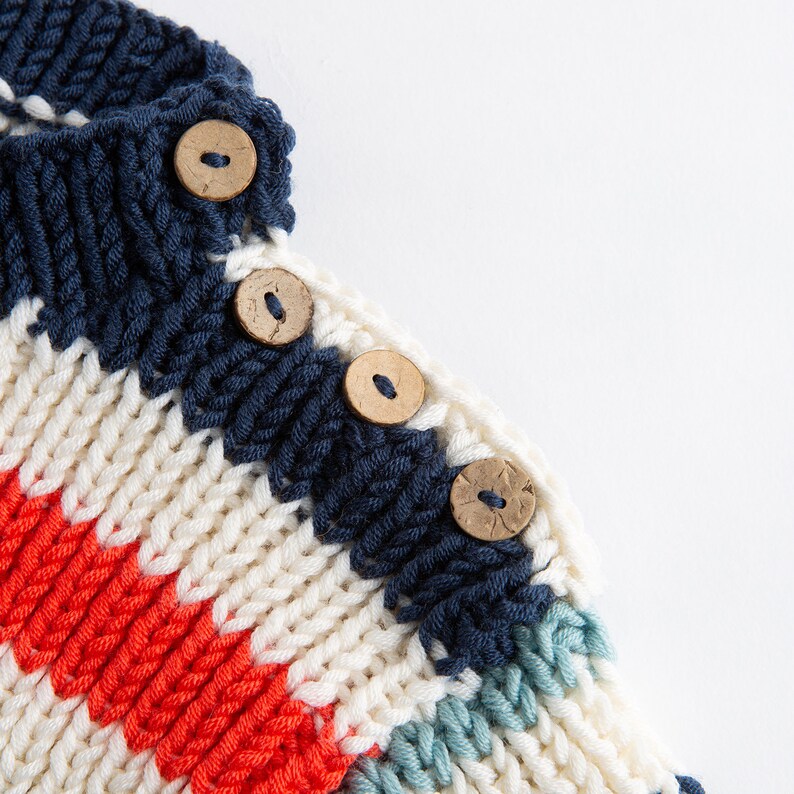 May include: Close-up of a striped knitted jumper with a white, red, blue and green colour scheme. The jumper has wooden buttons.