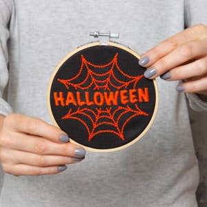 May include: A black embroidery hoop with a red spiderweb and the word "HALLOWEEN" embroidered in orange thread.