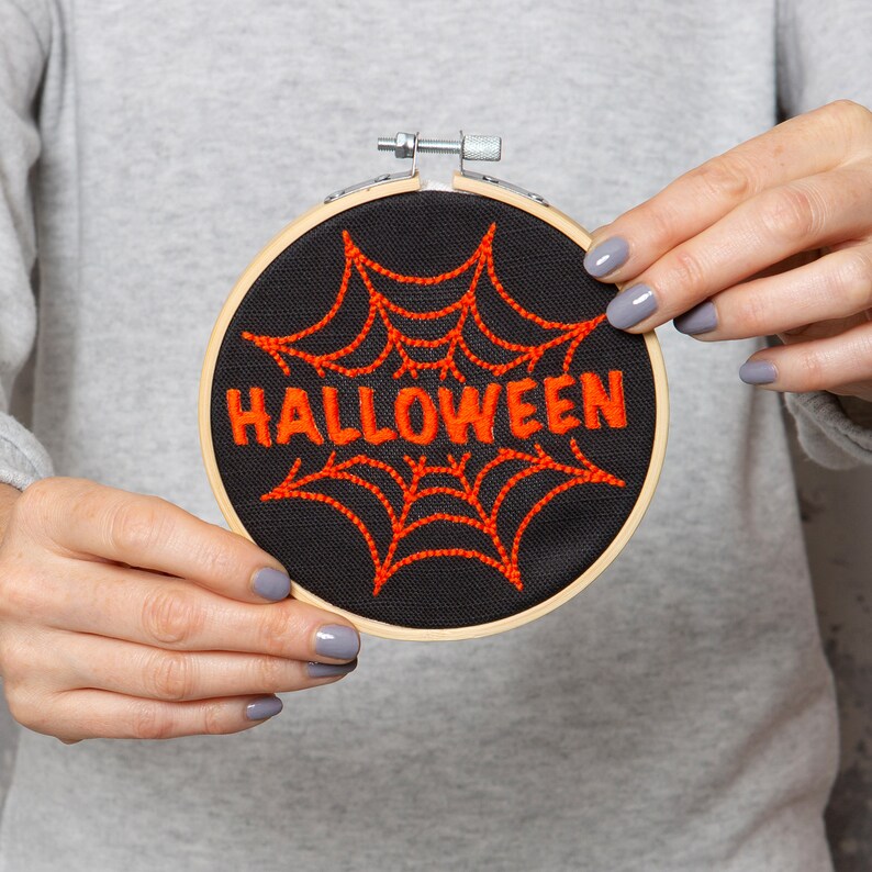 May include: A black embroidery hoop with a red spiderweb and the word "HALLOWEEN" embroidered in orange thread.