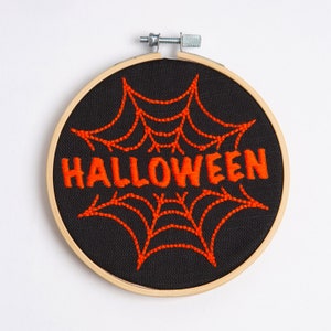 May include: Embroidered Halloween-themed hoop art with a black fabric background and an orange spiderweb design with the word "HALLOWEEN" in orange thread.