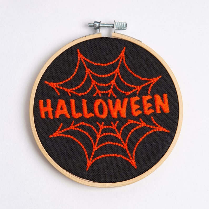 May include: Embroidered Halloween-themed hoop art with a black fabric background and an orange spiderweb design with the word "HALLOWEEN" in orange thread.