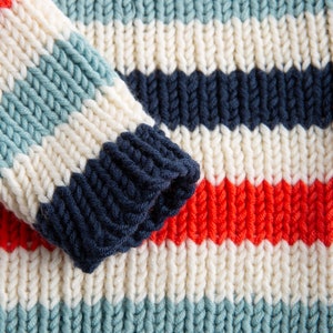 May include: A close-up of a knitted jumper with stripes of white, blue, red, and navy blue.