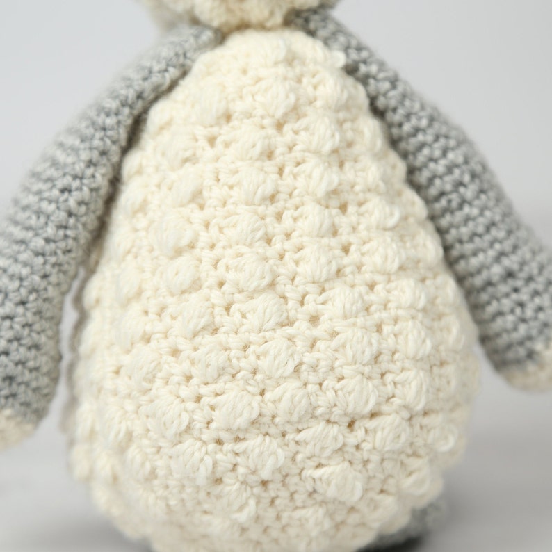 May include: A crocheted stuffed animal with a white body and gray arms. The body is made with a textured stitch that resembles sheep's wool.