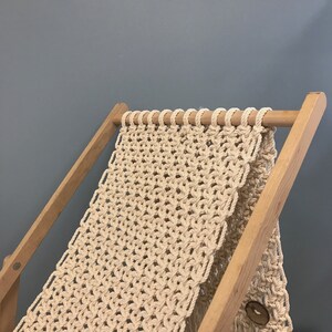 May include: A wooden frame with a macrame hammock woven from natural cream-colored cotton rope. The hammock is attached to the frame with wooden dowels.