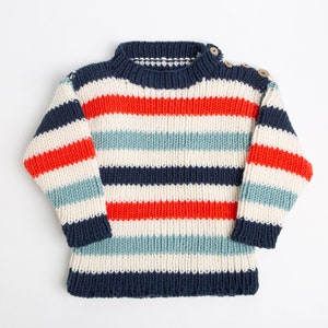May include: A striped knitted jumper in red, blue, white and cream colours. The jumper has a round neckline and long sleeves.