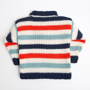 May include: A striped knitted jumper with a high neck. The jumper is white, red, blue, and light blue.