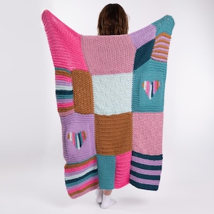 May include: A vibrant patchwork blanket with a variety of textures and patterns. The blanket displays squares of pink, teal, brown, and lavender, with striped and heart-shaped embroidered details. The blanket is held up, displaying its design.