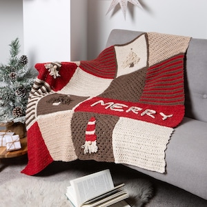 May include: A crocheted throw blanket with a patchwork design featuring red, brown, and cream squares. The blanket has a "Merry" inscription and various Christmas-themed motifs, including a tree and a candy cane.
