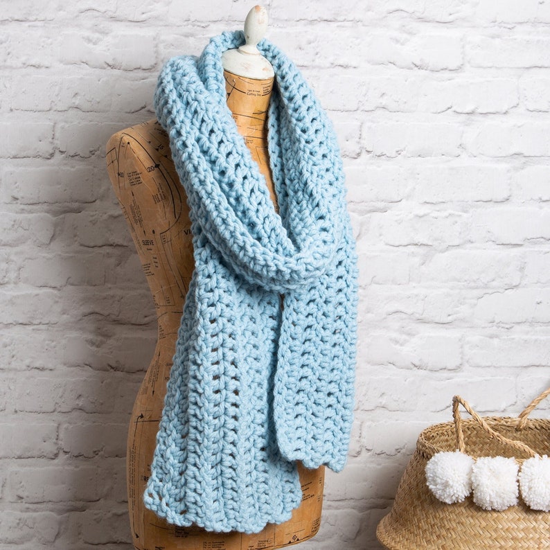 Puede incluir: Una bufanda de crochet azul claro drapeada sobre un maniqu&iacute;. La bufanda est&aacute; hecha con un patr&oacute;n de punto simple y tiene una forma larga y fluida.