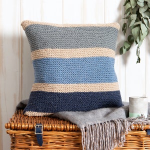 K&ouml;nnte beinhalten: Ein quadratisches Strickkissen mit horizontalen Streifen in den Farben Beige, Hellblau, Mittelblau und Dunkelmarineblau. Das Kissen weist durchgehend ein strukturiertes kraus rechts gestricktes Muster auf, das eine einheitliche Oberfl&auml;che bildet.