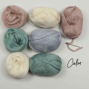 May include: Six balls of yarn in various shades of pink, blue, and white. The yarn is arranged in a circle with a needle and the word "Calm" written in cursive.