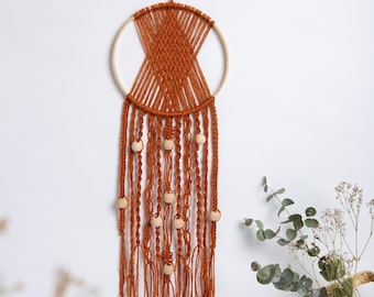 May include: A handcrafted, burnt orange macrame dream catcher. The circular design features a wooden hoop, intricate woven patterns, and hanging strands adorned with wooden beads. This bohemian-style wall decor adds a touch of natural warmth.