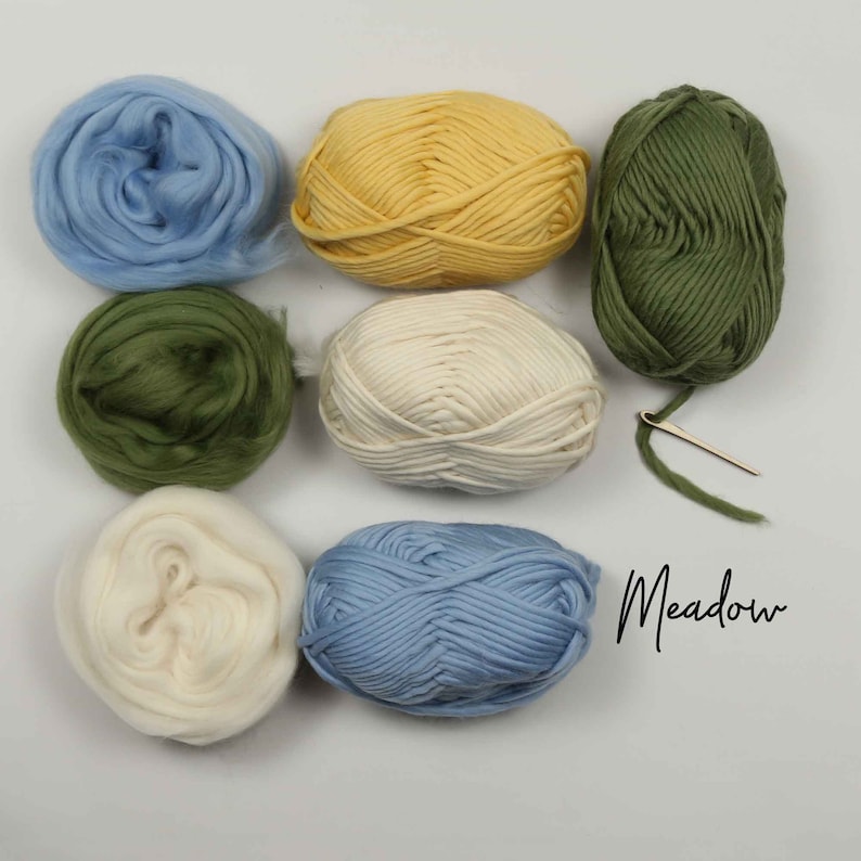 May include: Six balls of yarn in various colors, including blue, green, yellow, and white. The yarn is arranged in a circle on a white surface. A small needle is also included. The text "Meadow" is written in cursive on the right side of the image.