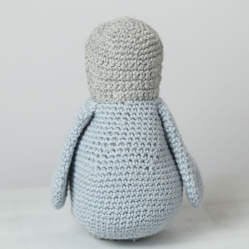 May include: A crocheted penguin toy with gray and light blue yarn. The penguin is standing upright with its wings out to the sides.