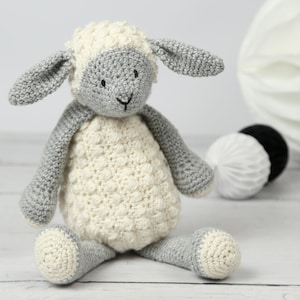 May include: A crocheted stuffed lamb toy with a white body and gray legs, ears, and head. The lamb has black eyes and a black nose.