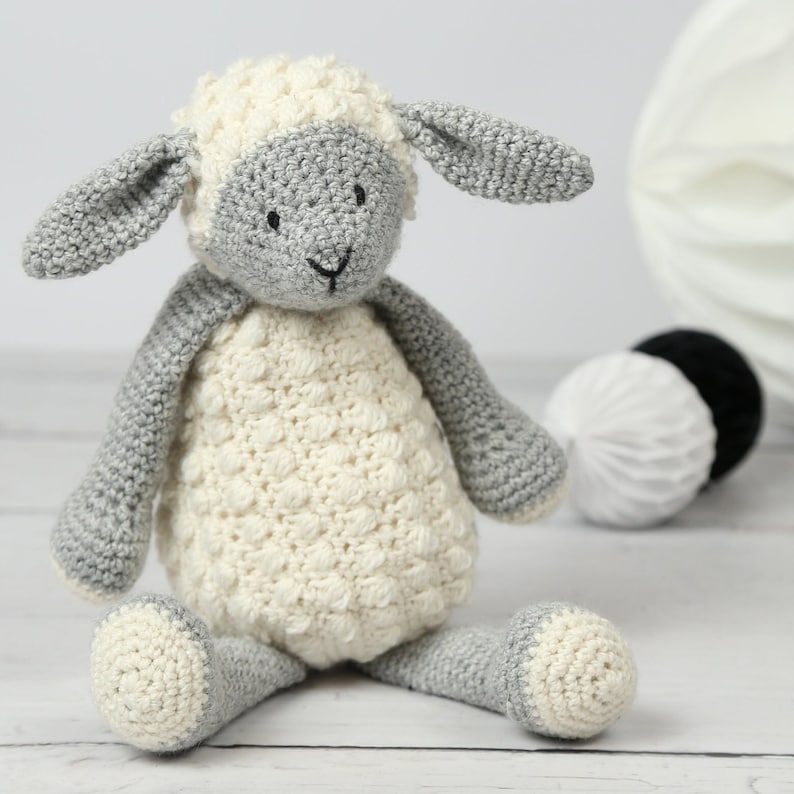 May include: A crocheted stuffed lamb toy with a white body and gray legs, ears, and head. The lamb has black eyes and a black nose.