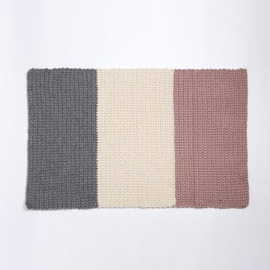 May include: A rectangular crocheted rug with three vertical stripes in gray, white, and pink.