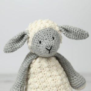 May include: A crocheted stuffed lamb toy with a white body and gray face and ears. The lamb has black eyes and a small black nose.