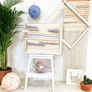 May include: A white wooden loom with two woven wall hangings, one with a geometric pattern and the other with a more free-form design.  There are three balls of yarn in different colors, including pink, blue, and white.  The text "Wool Couture" is visible on a white sign.