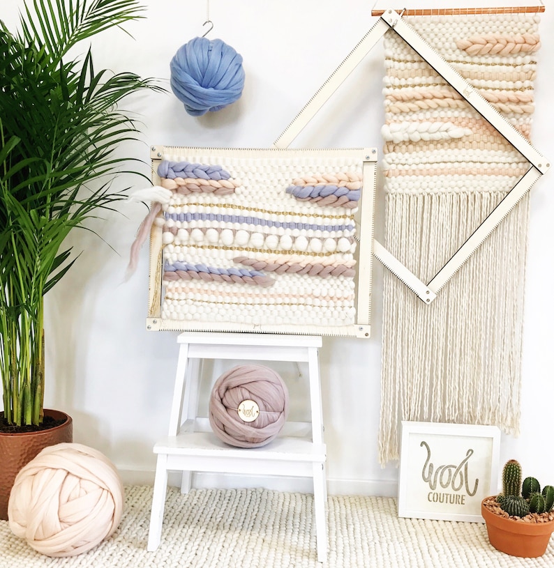 May include: A white wooden loom with two woven wall hangings, one with a geometric pattern and the other with a more free-form design.  There are three balls of yarn in different colors, including pink, blue, and white.  The text "Wool Couture" is visible on a white sign.