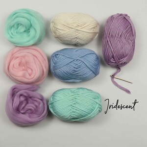 May include: Six balls of yarn in various pastel colors, including pink, light blue, lavender, and green. The yarn is arranged in a circle on a white surface. The word "Iridescent" is written in black ink below the yarn.