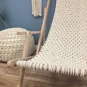 May include: A white macrame hammock chair with a wooden frame. The chair is made of thick rope and has a woven pattern. The chair is sitting on a wooden floor.