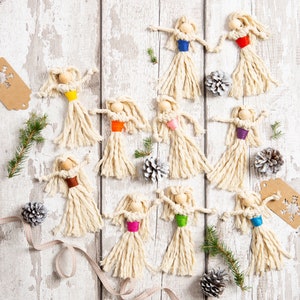 May include: Nine handmade string dolls with different coloured yarn accents. The dolls are hanging from a white wooden background.