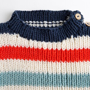 May include: A striped knitted jumper with a navy blue neckline and white, red, and blue stripes.