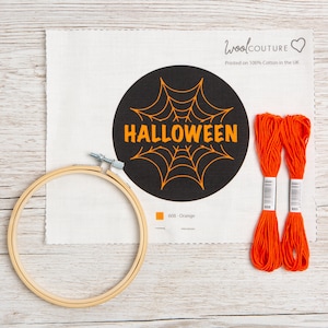 May include: A cross-stitch kit featuring a black circle with a spiderweb and the word "HALLOWEEN" in orange. The kit includes a piece of white fabric, a wooden embroidery hoop, and two spools of orange embroidery floss.