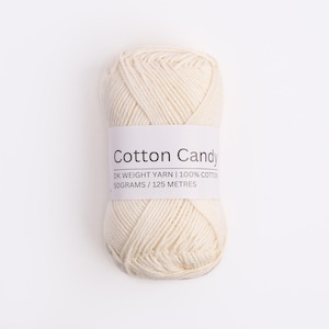 May include: A skein of off-white DK weight yarn made of 100% cotton. The label reads Cotton Candy, DK WEIGHT YARN, 100% COTTON, 50GRAMS / 125 METRES. The yarn is wound into a compact, oval-shaped ball with visible twisted strands of fiber.