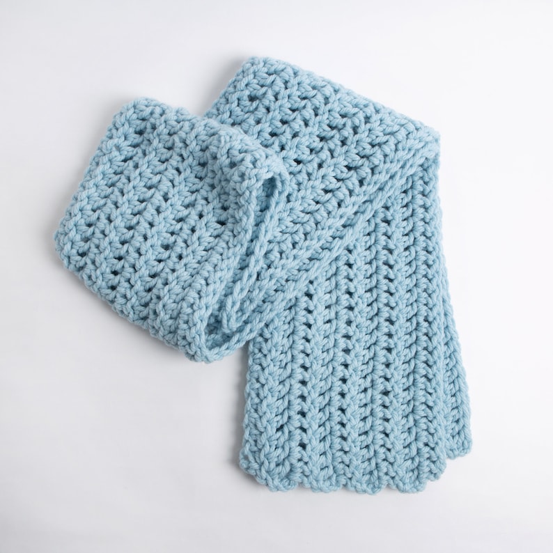 Puede incluir: Una bufanda de crochet azul claro con un patr&oacute;n texturizado.