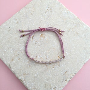 May include: A delicate pink suede bracelet with a row of small, light pink beads and gold accents.