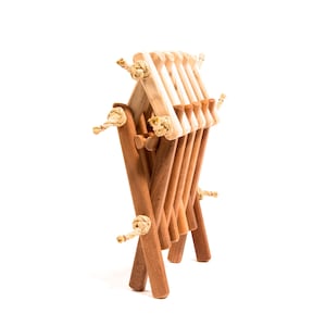 May include: A wooden folding chair with a natural finish. The chair is made of multiple pieces of wood that are connected by rope.