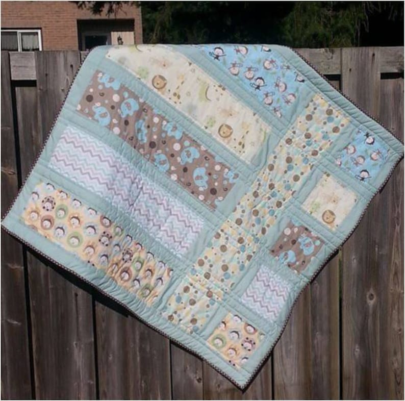 May include: A baby quilt with a patchwork design featuring various animal prints, including owls, giraffes, and monkeys. The quilt is made with a variety of fabrics in shades of blue, brown, and white.
