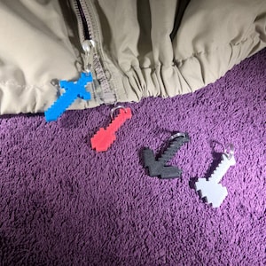May include: Four pixelated Minecraft-themed keychains: a blue sword, a red pickaxe, a black axe, and a gray pickaxe.
