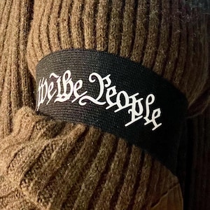 May include: A black elastic band with the words "We the People" printed in white.