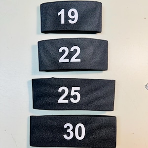 May include: Four black elastic bands with white numbers printed on them. The numbers are 19, 22, 25, and 30.