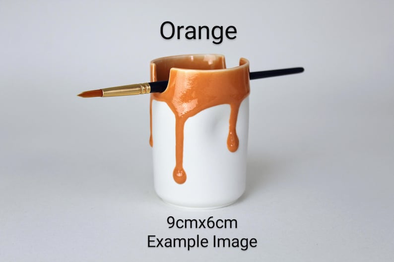 May include: Orange ceramic brush holder with a drip glaze design. The holder is 9cm x 6cm and is shown with a paintbrush.