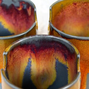 May include: Three ceramic mugs with a drip glaze in shades of gray, yellow, and red.