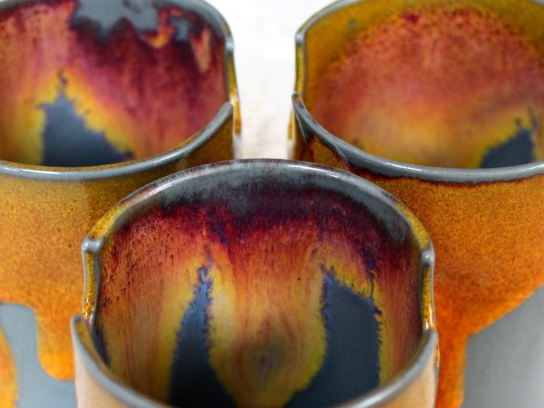 May include: Three ceramic mugs with a drip glaze in shades of gray, yellow, and red.