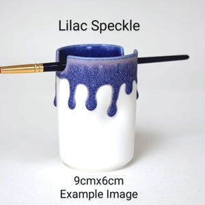 May include: A white ceramic brush holder with a blue and purple speckled glaze. The glaze drips down the sides of the holder. The holder is 9 cm by 6 cm. Lilac Speckle Example Image